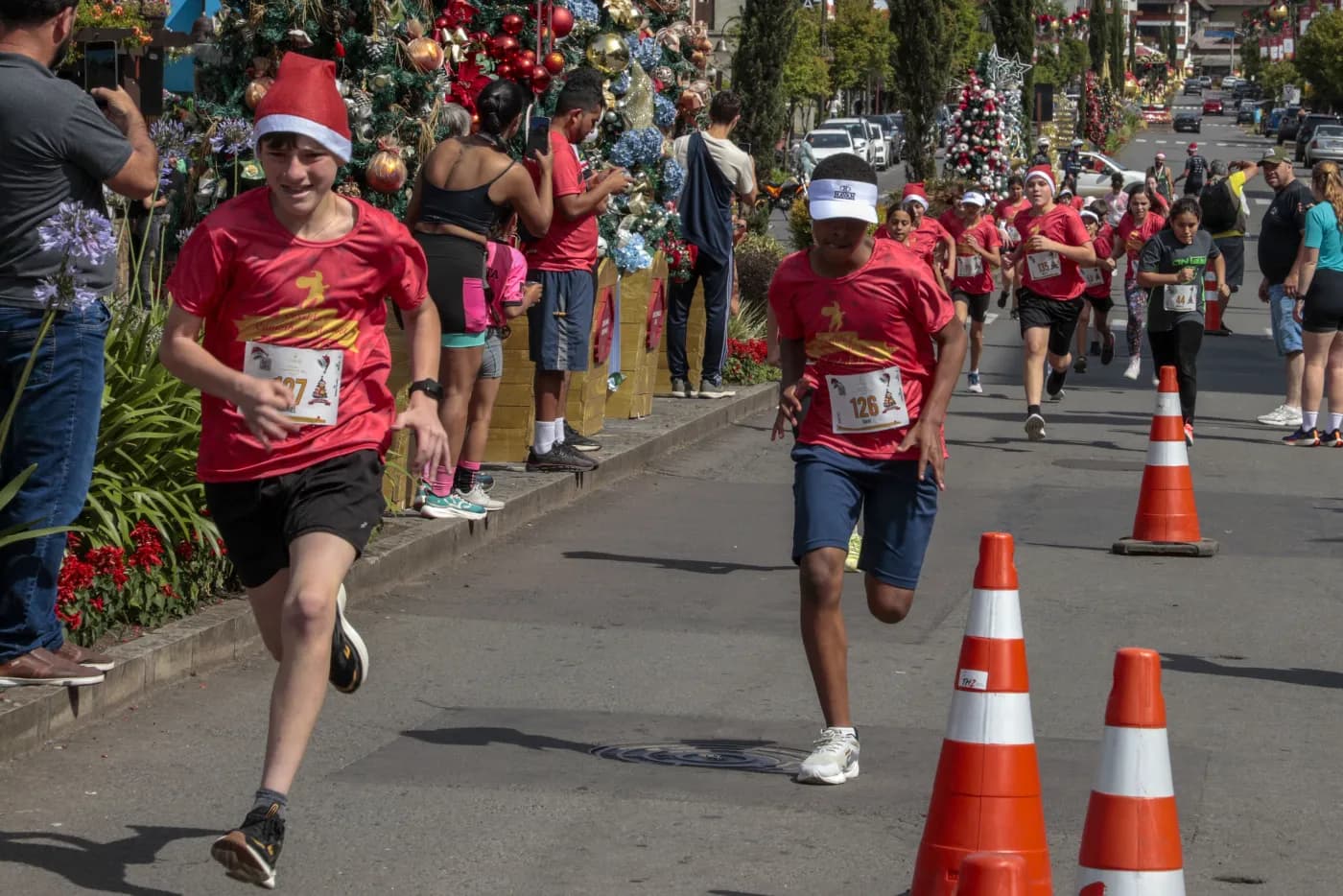 Dois adolescentes disputam a chegada da Corrida Kids na pista sinalizada por cones.