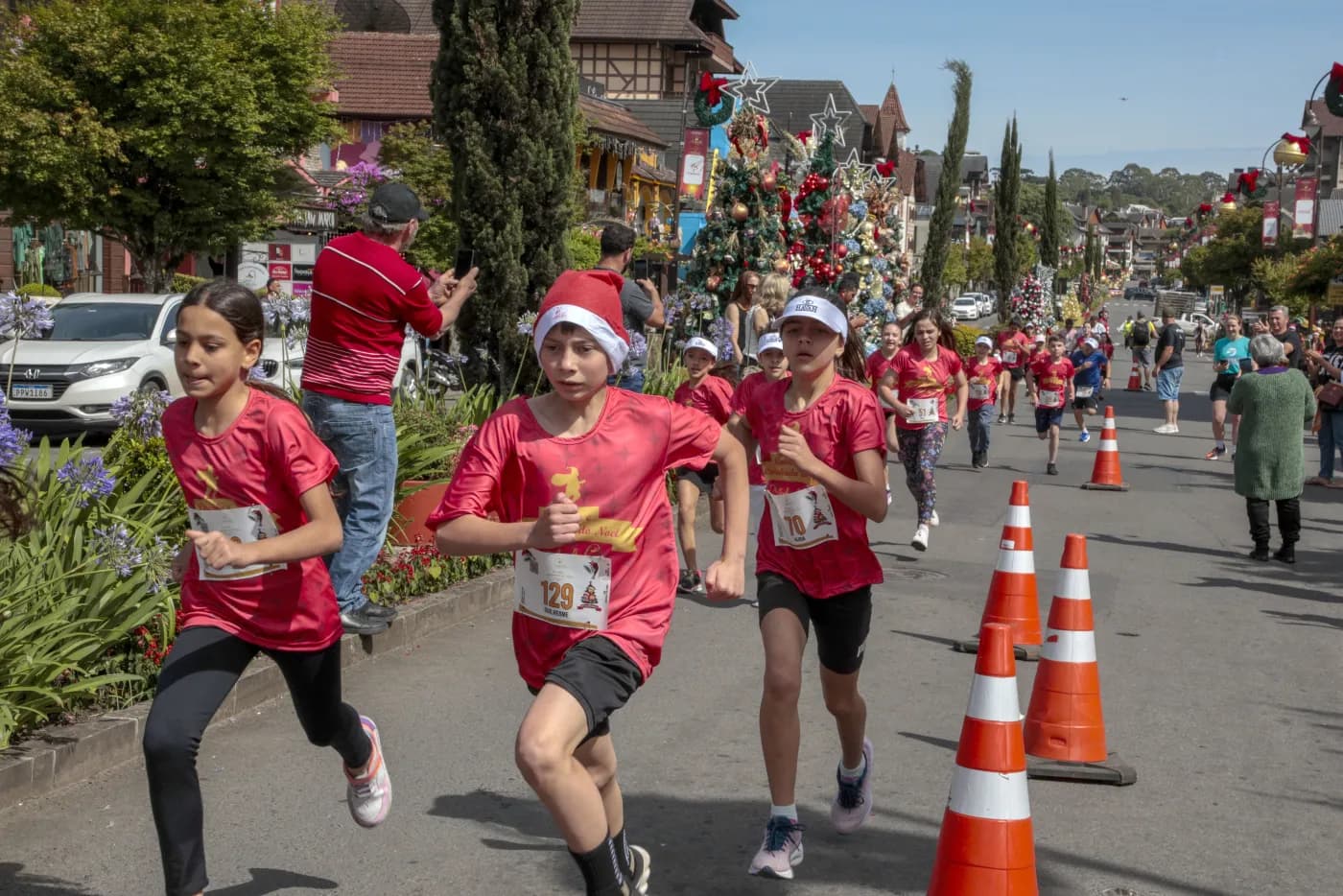 Crianças correndo lado a lado na Corrida Kids, uma delas de gorro de Papai Noel.