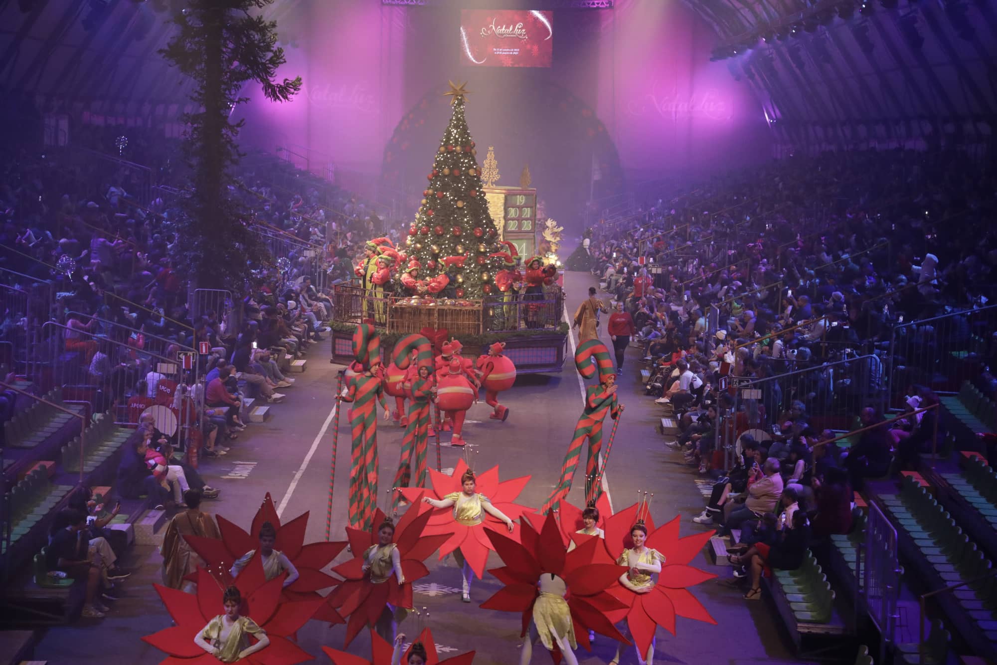Plateia lotada acompanhando o Grande Desfile de Natal em Gramado, com a árvore iluminada ao fundo